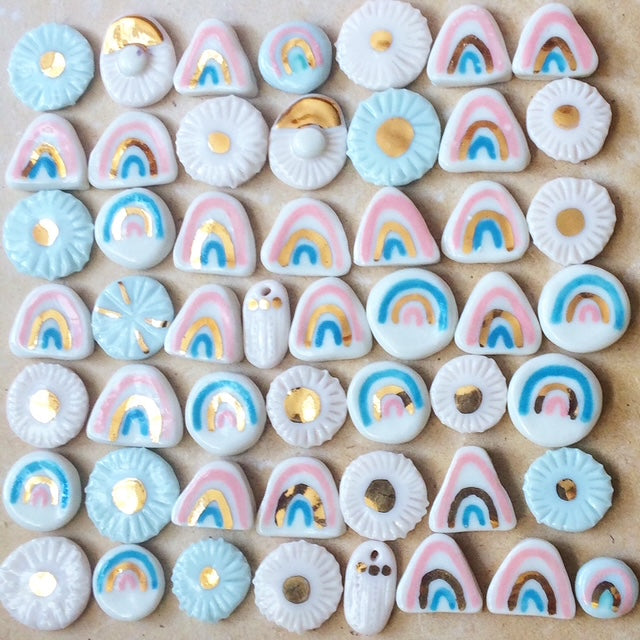 Collection of colorful ceramic charms with rainbow and heart designs on a wooden surface.