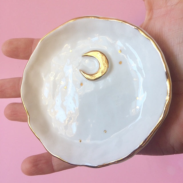 White ceramic dish with gold rim held by a hand against a pink background