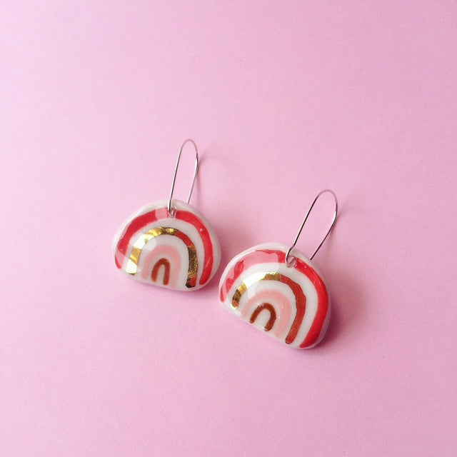Pair of earrings with red, white, and gold design on a pink background