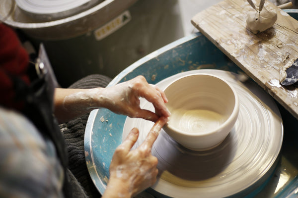 A person using a pottery wheel to shape a bowl out of clay.

