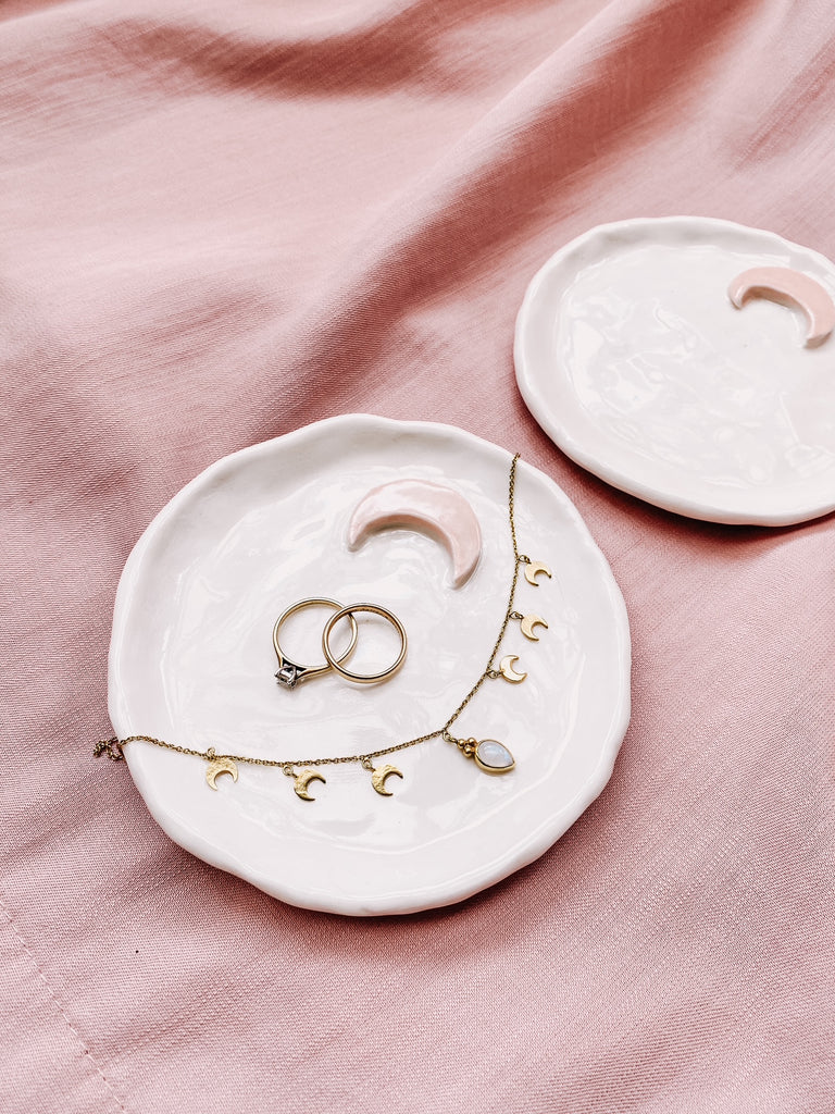 White ceramic jewelry dish with gold jewelry on a pink fabric background