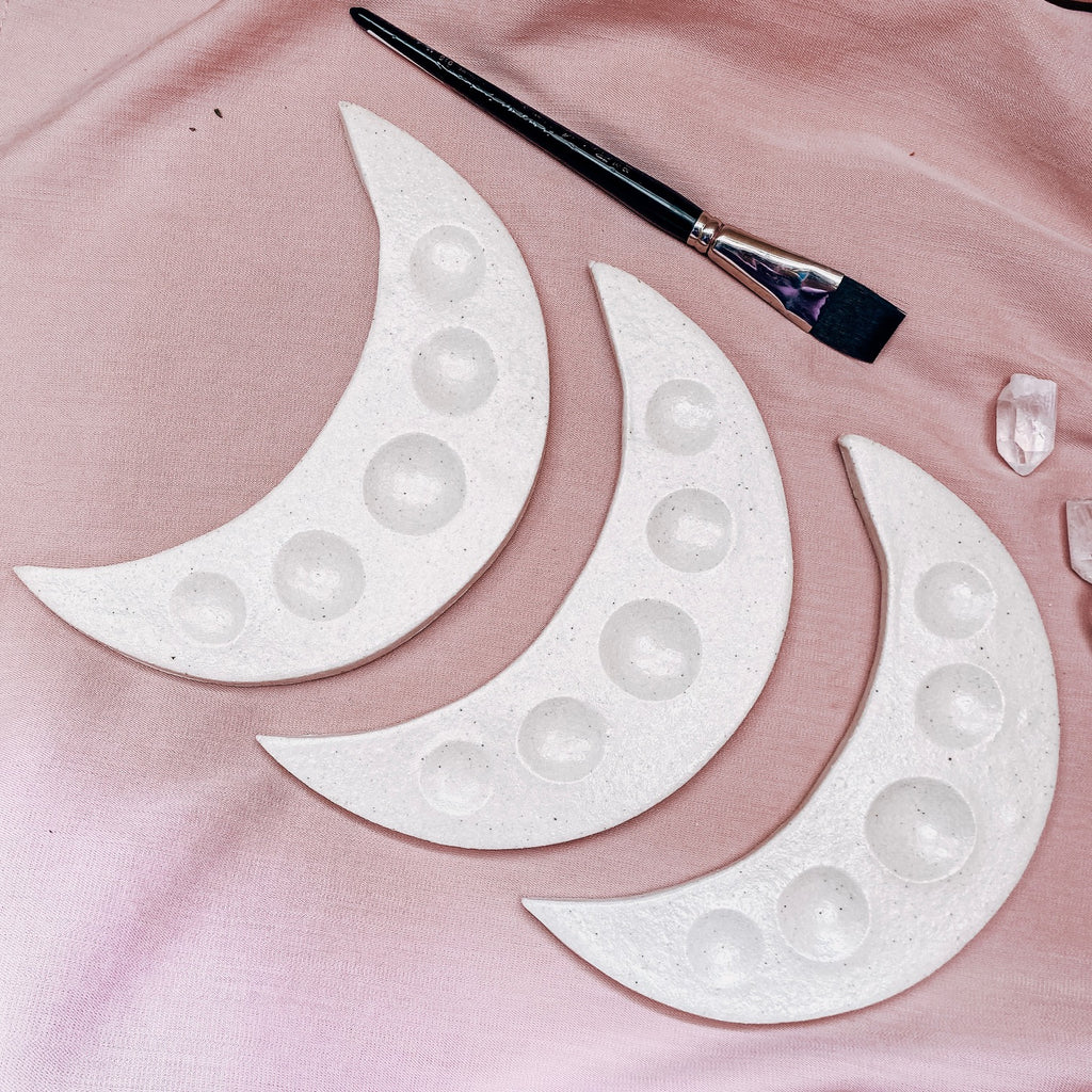 Decorative moon-shaped pieces with embedded stones on a pink surface, accompanied by a paintbrush.