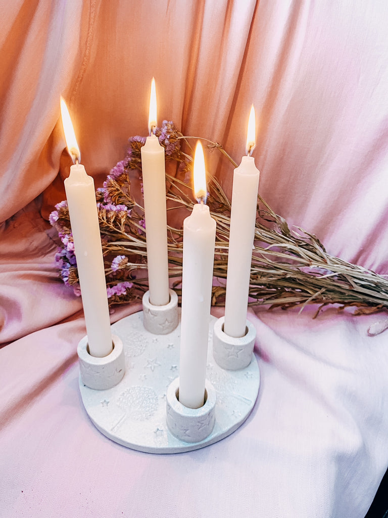 Candle holder with four lit candles on a pink fabric background